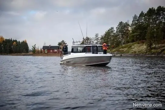 A fishing boat is on a calm lake with two people onboard, trees and a red cabin visible on the shore.